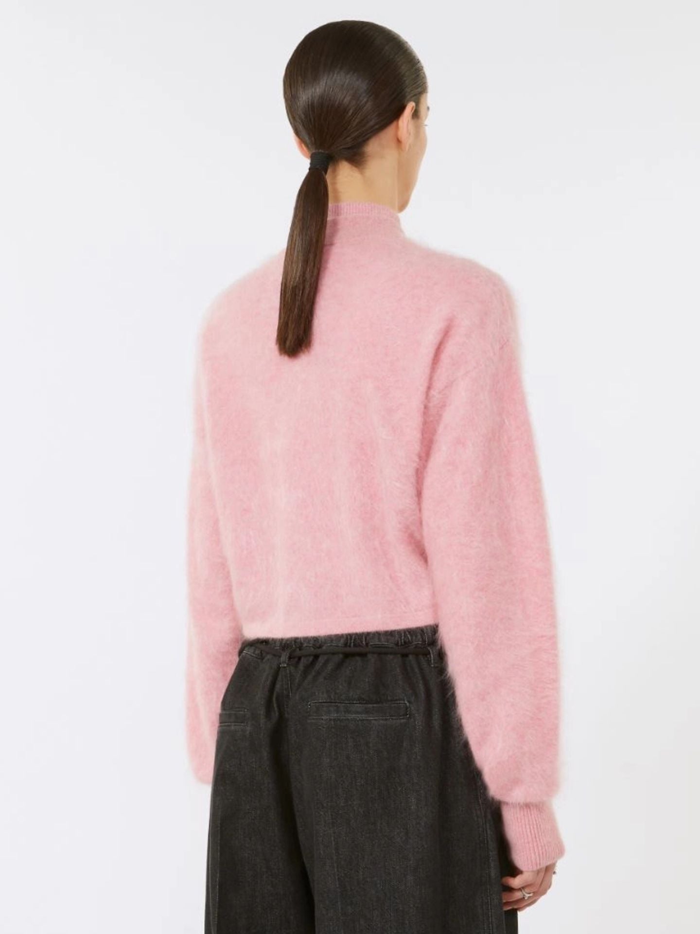 Person wearing a pink sweater and dark pants on a white background