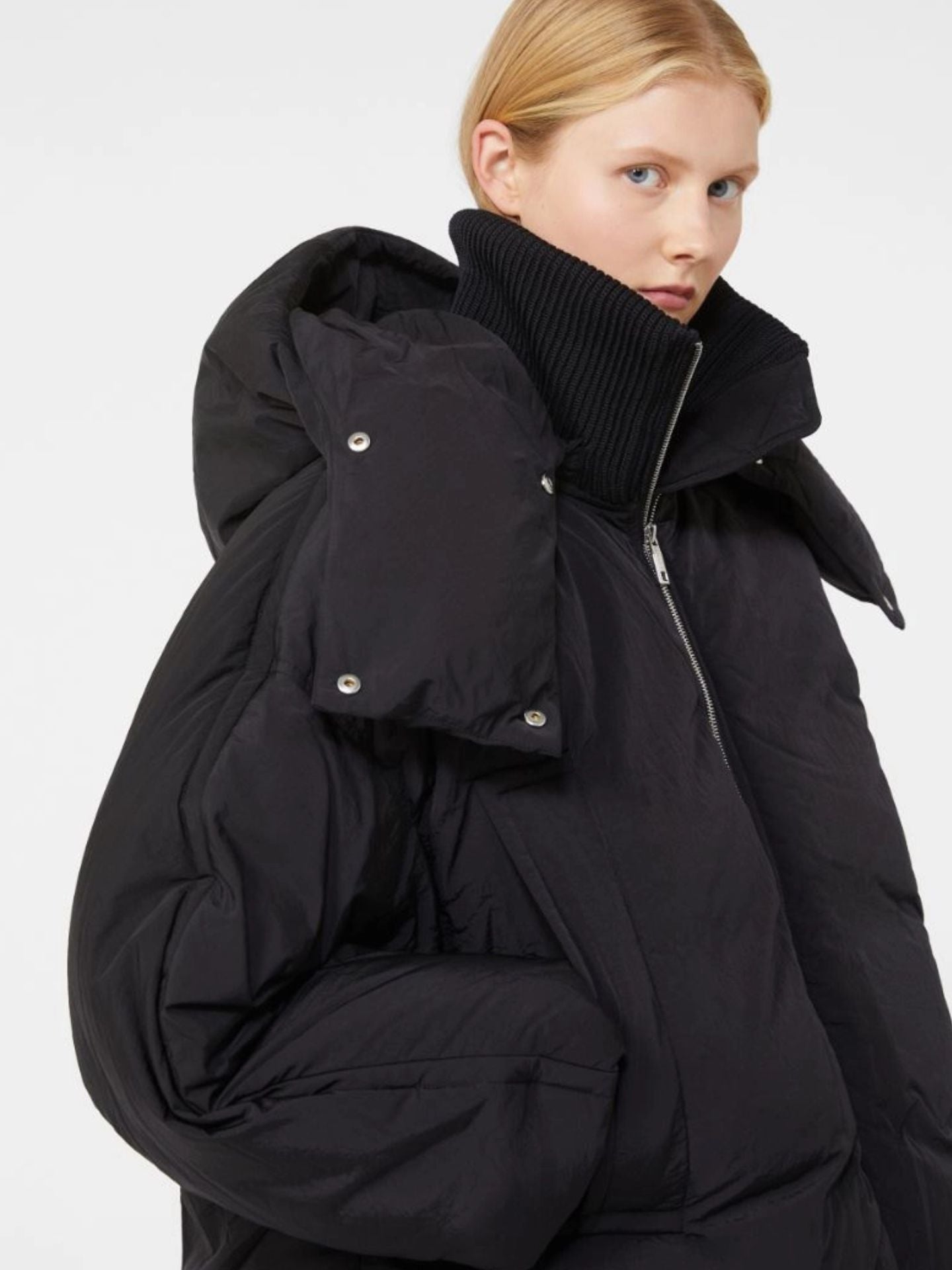 Person wearing a black puffer coat with a hood on a white background