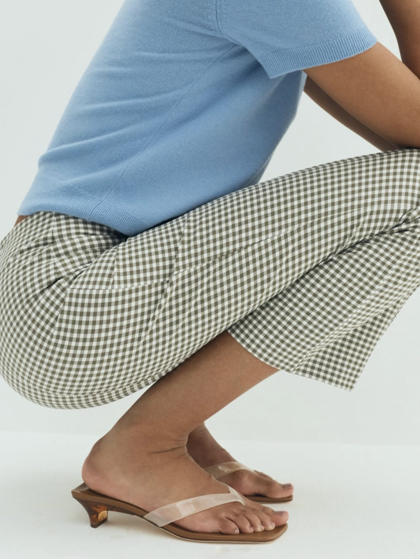 Person wearing a blue shirt and checkered pants with beige sandals on a white background
