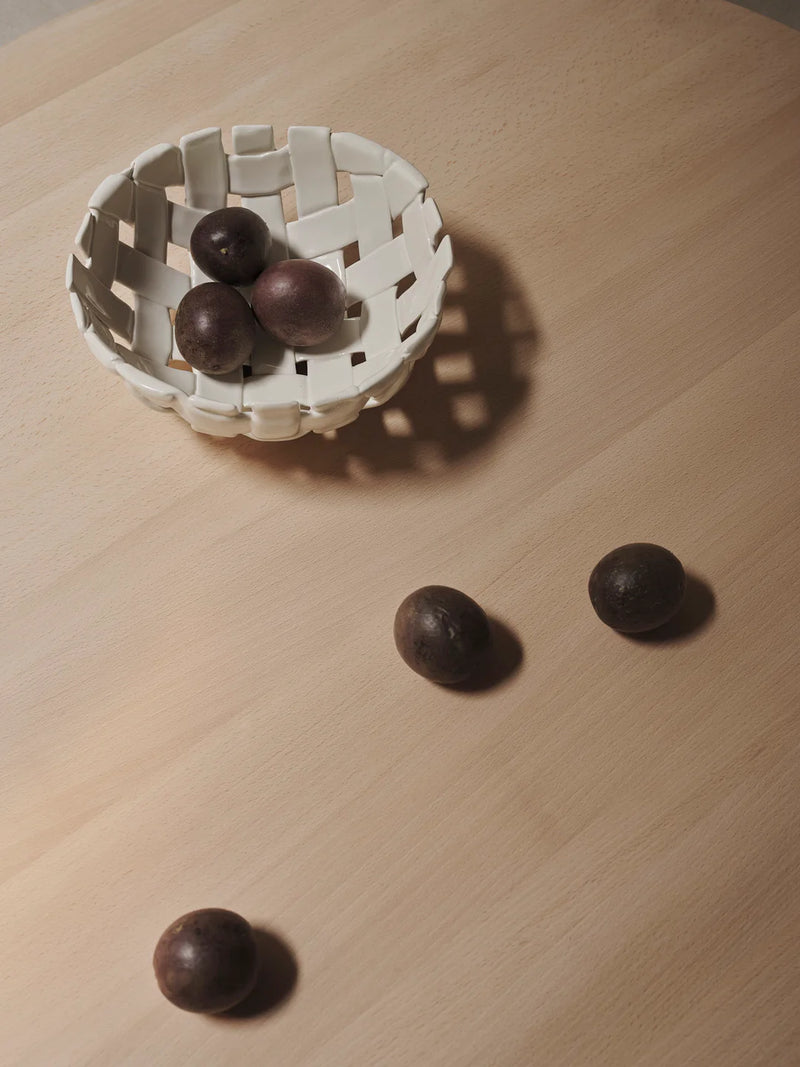 Small white woven basket with dark fruits on a wooden surface.