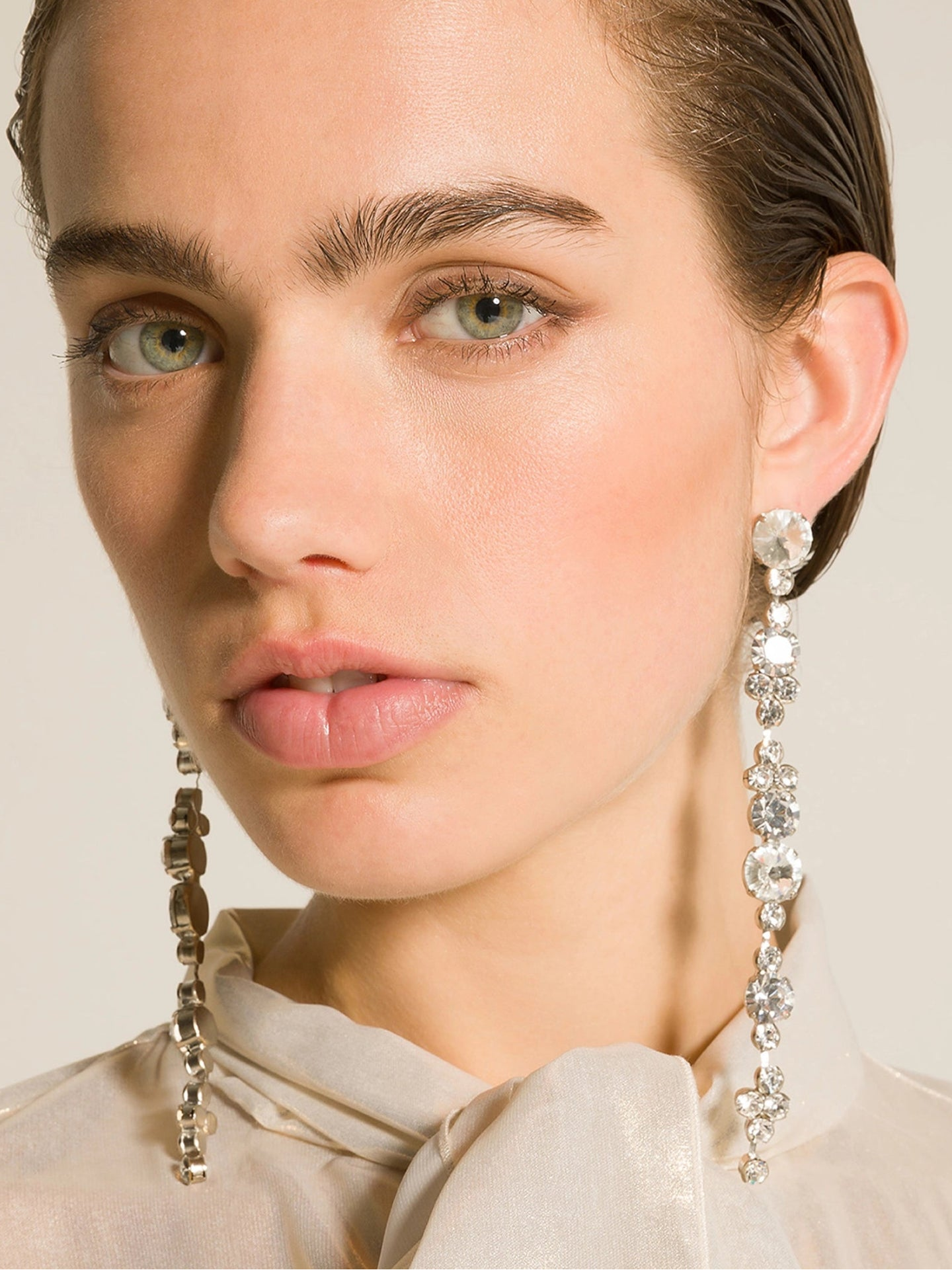 Close-up of a person wearing sparkling earrings against a neutral background