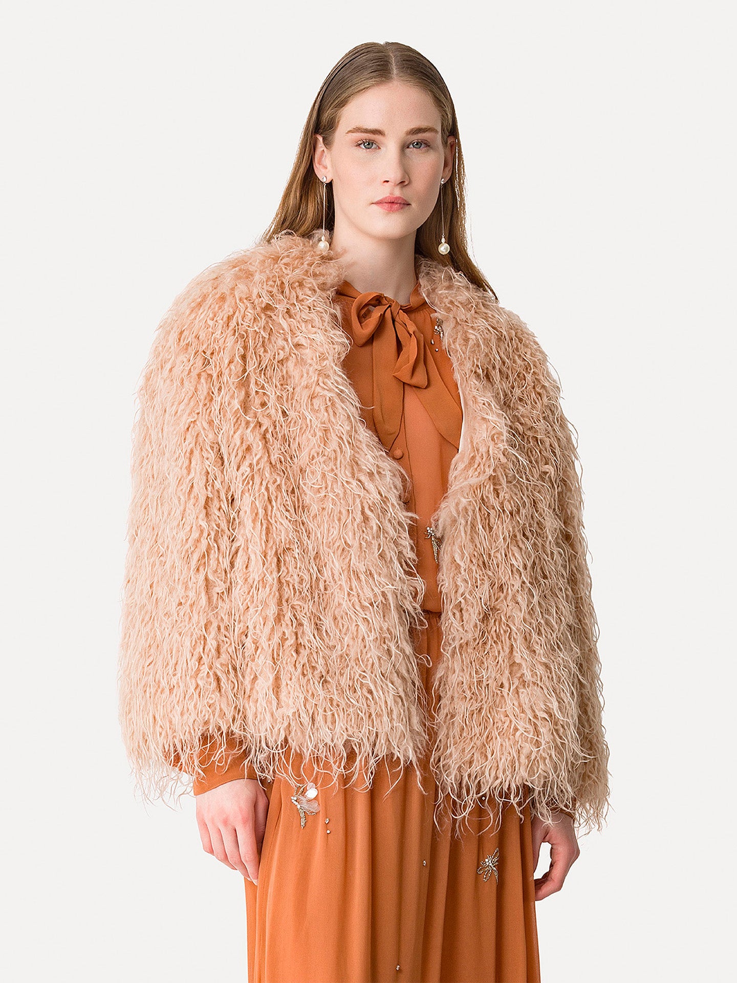 Woman wearing a beige fluffy jacket over an orange dress on a white background