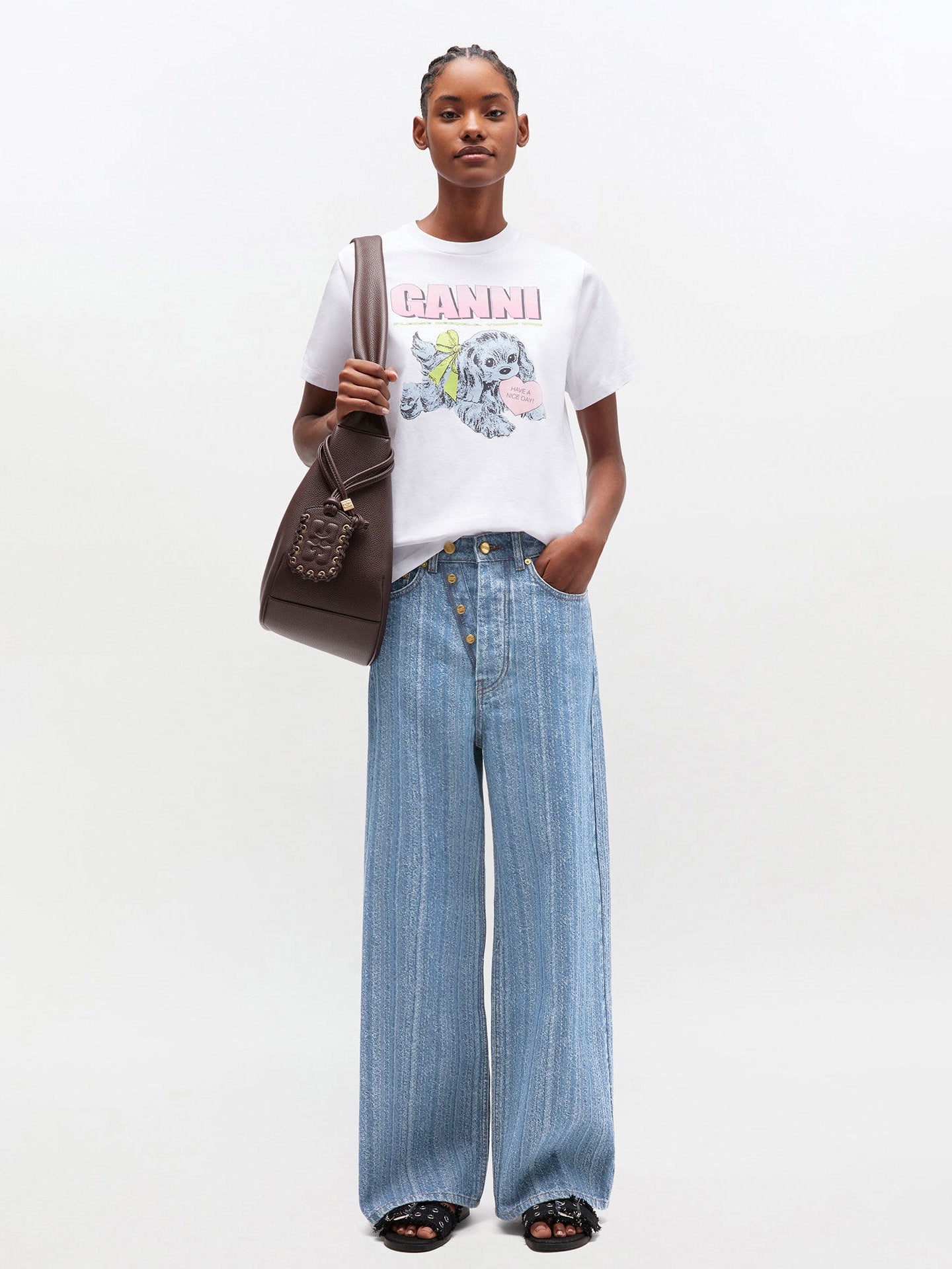 Woman wearing a white t-shirt with a graphic design and blue jeans, holding a brown bag on a white background