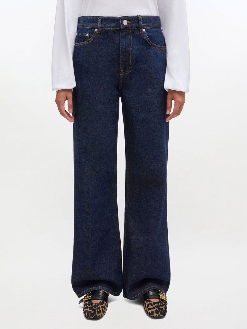 Person wearing dark blue jeans with a white shirt on a light gray background
