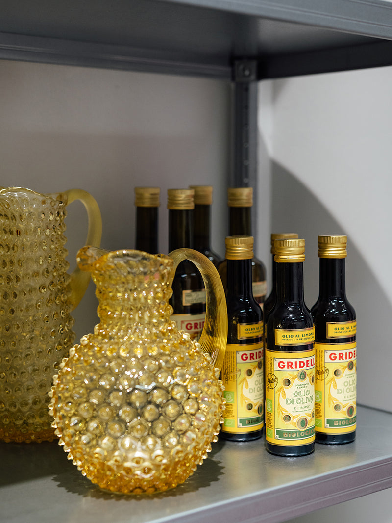 A shelf display featuring several bottles of Gridelli extra virgin lemon olive oil alongside decorative textured glass pitchers.