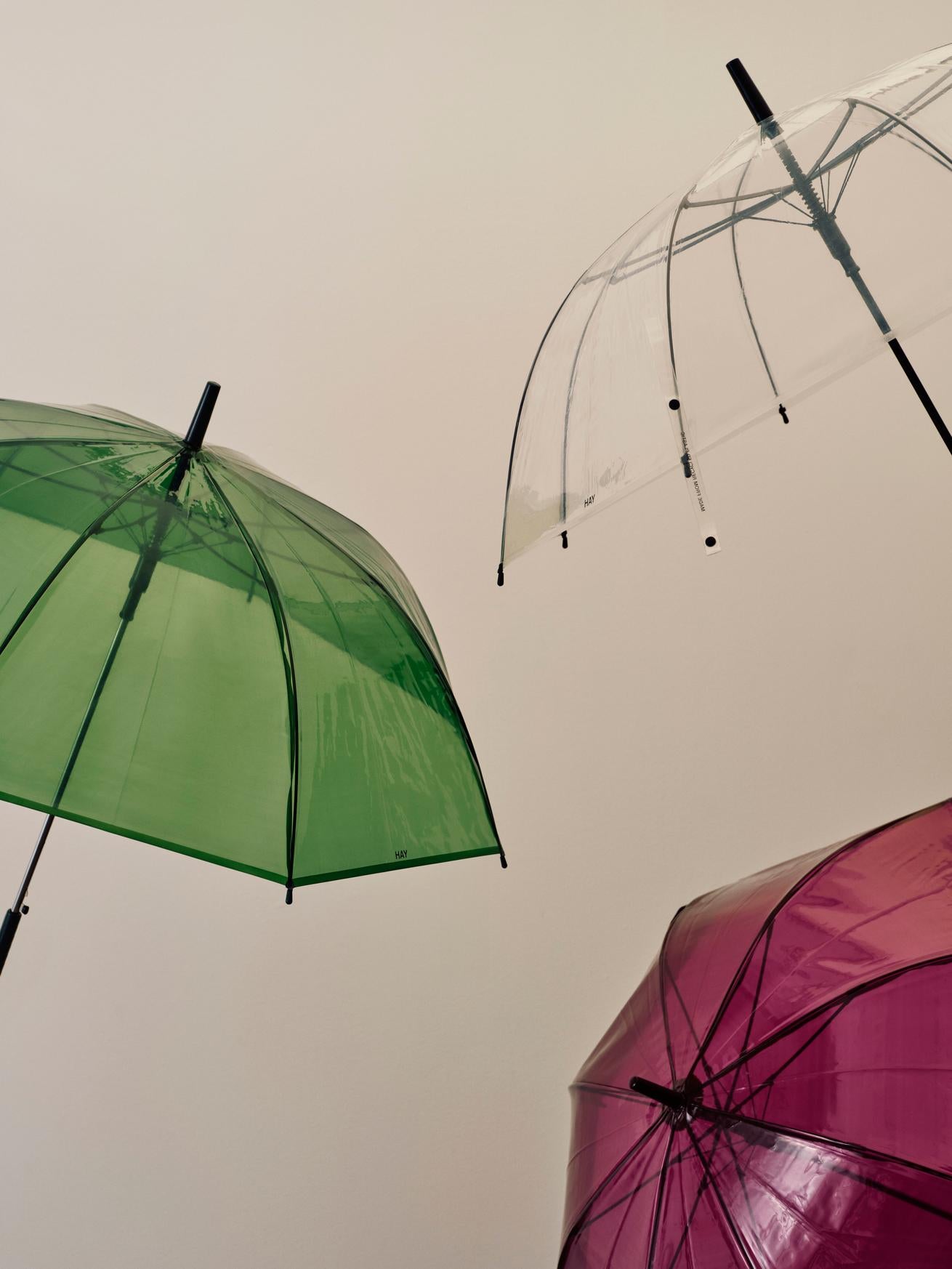 Green, clear, and pink umbrellas against a beige background