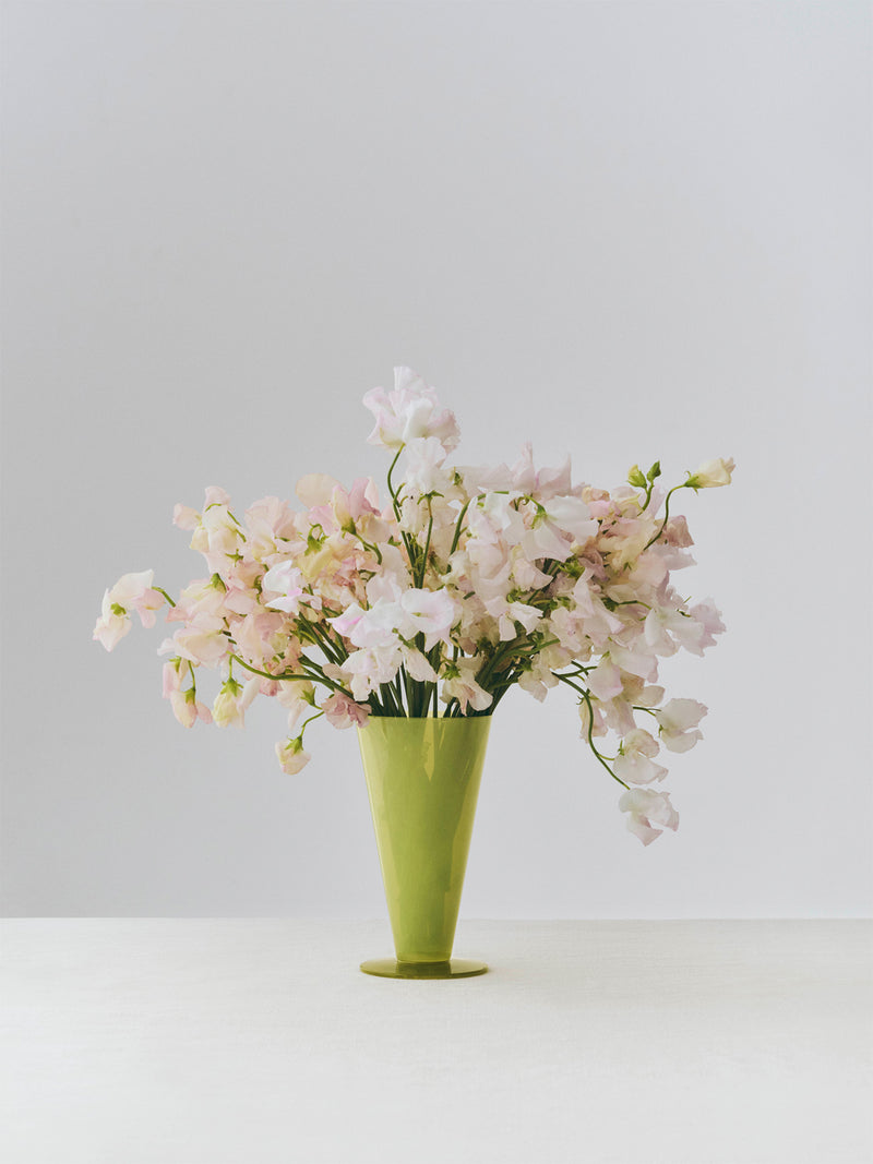 Green vase with pink flowers on a white surface and light gray background