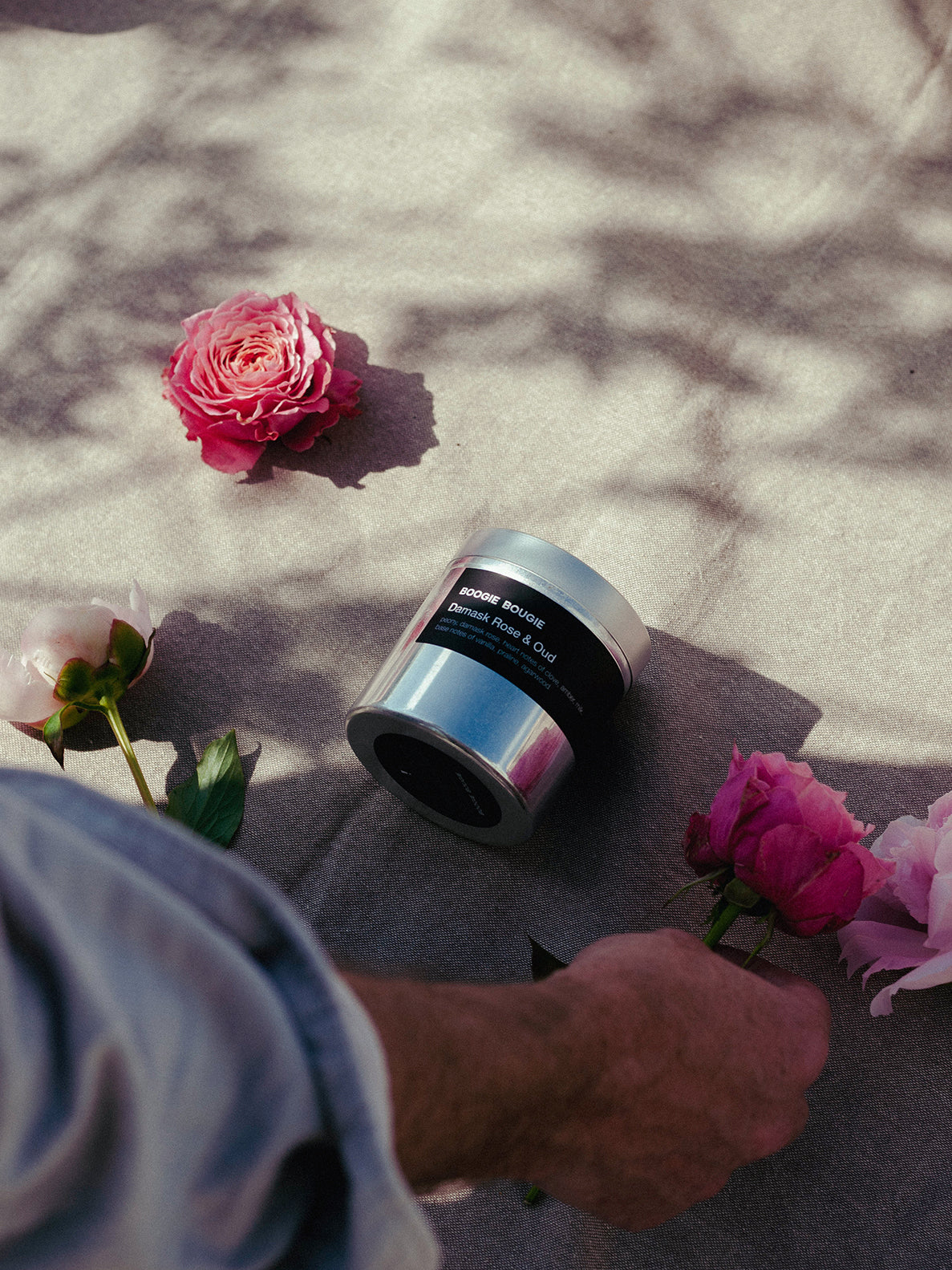 Silver jar with black lid on a textured surface surrounded by pink roses