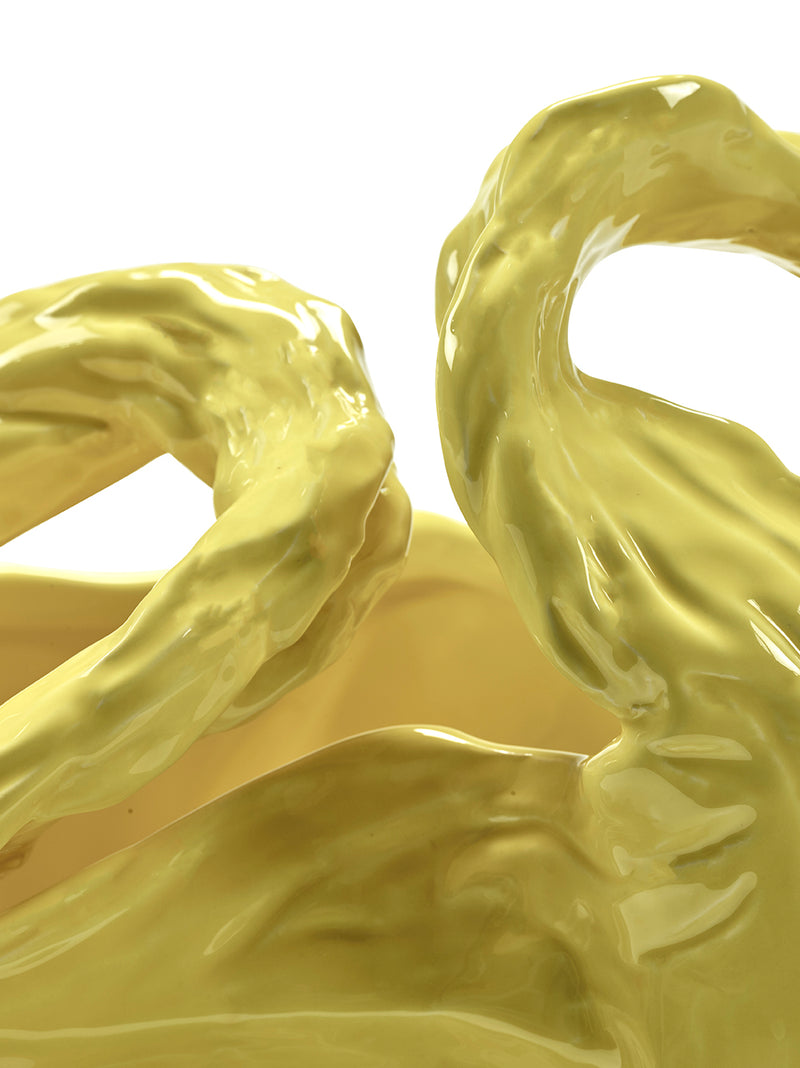Yellow ceramic sculpture of intertwined forms on a white background