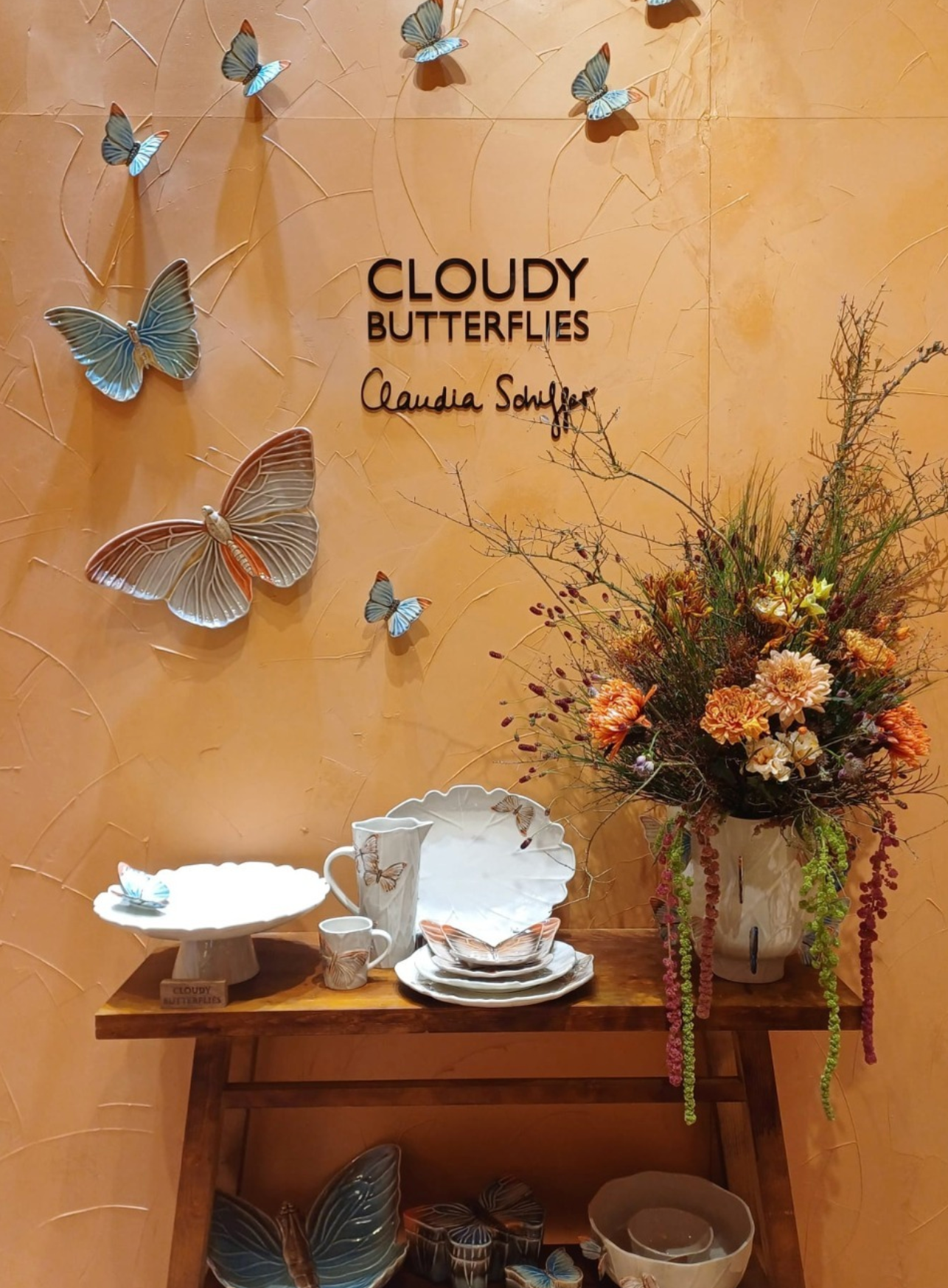 Decorative setting with butterflies, flowers, and ceramic items against a wall with 'Cloudy Butterflies' text.