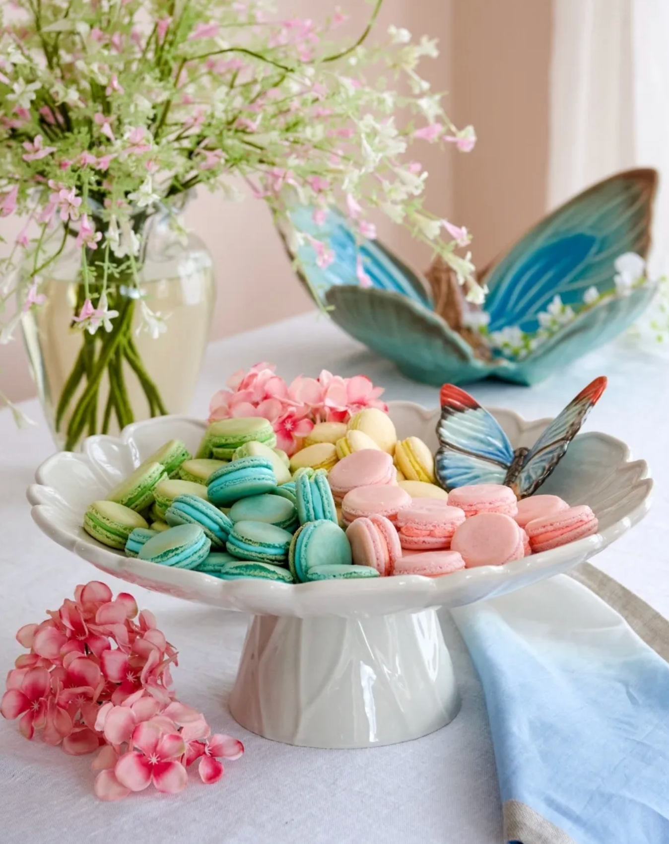 Colorful macarons on a white cake stand with flowers and butterfly decorations.