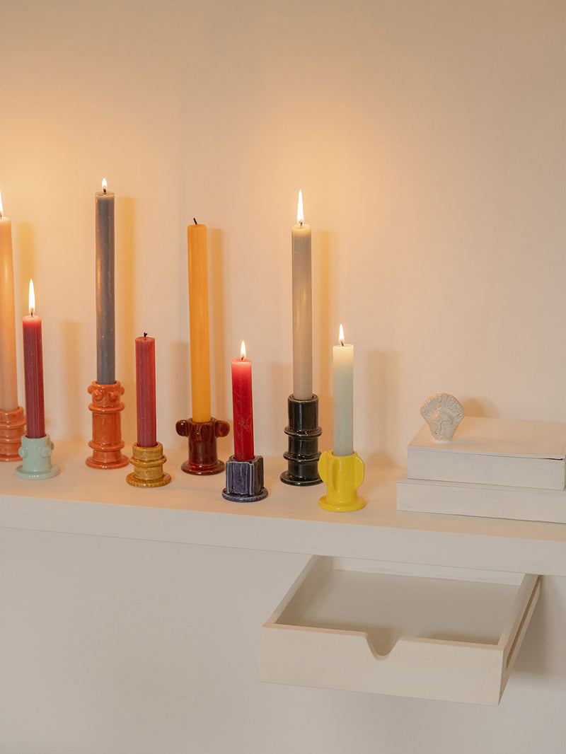 Colorful candles & their holders on a shelf with a neutral background