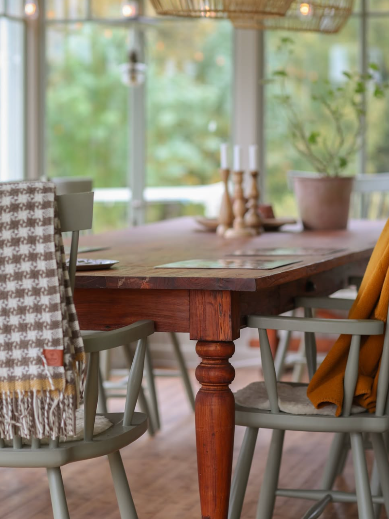 Dining room with wooden table and chairs near large windows with a view of greenery.