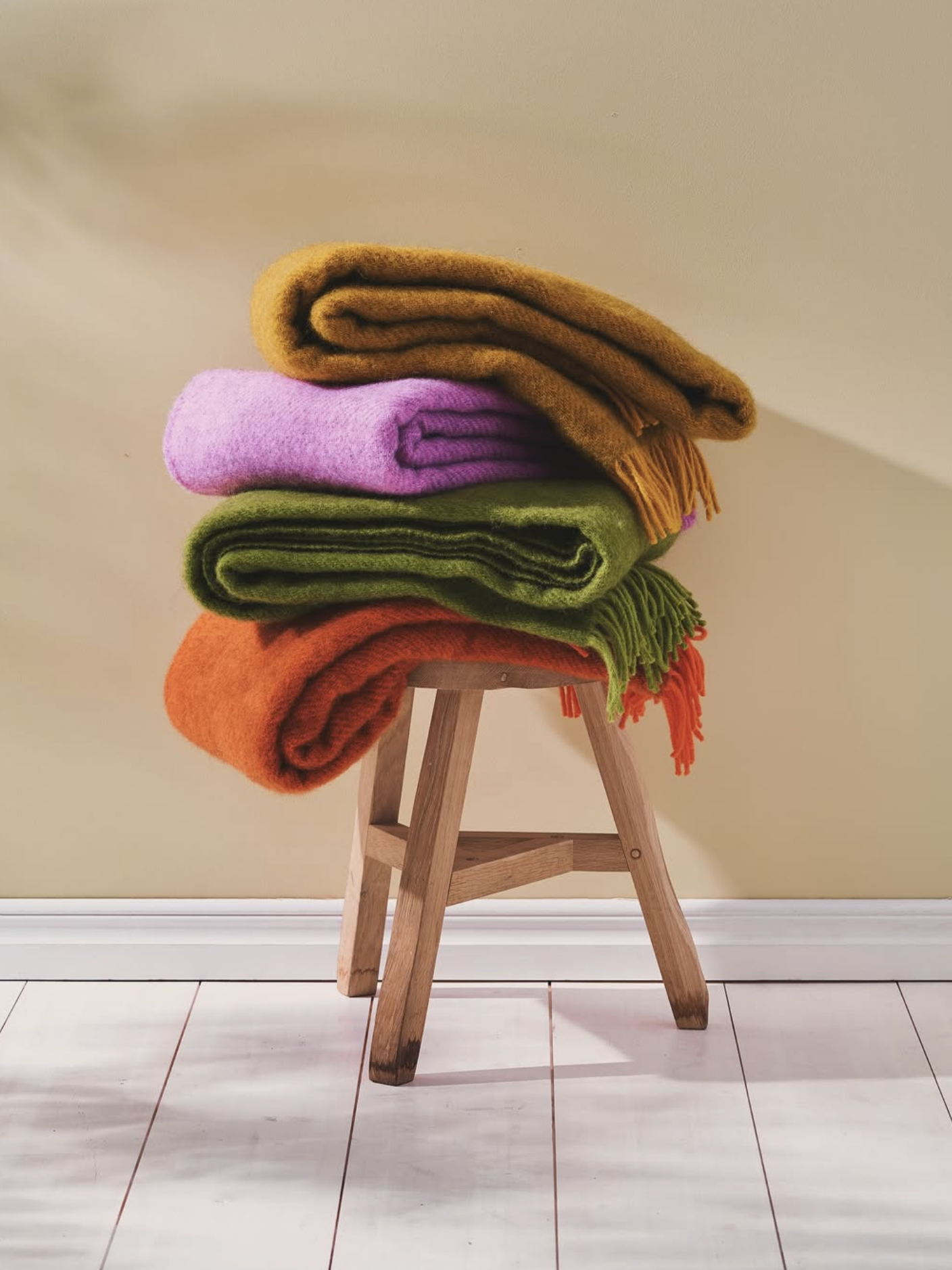 Stack of colorful folded blankets on a wooden stool against a beige wall.