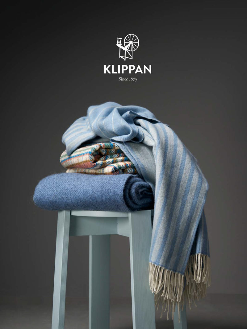 Stack of folded blankets on a stool with Klippan logo above