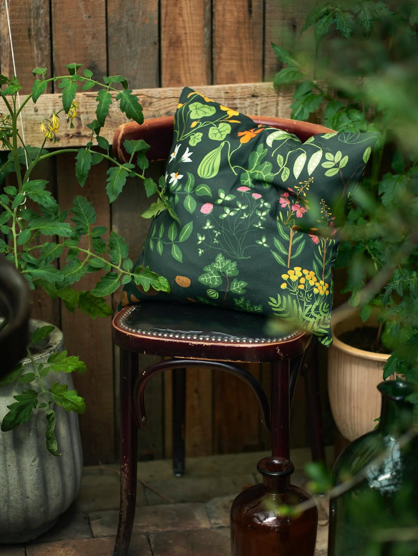 Decorative pillow with floral pattern on a wooden chair surrounded by plants