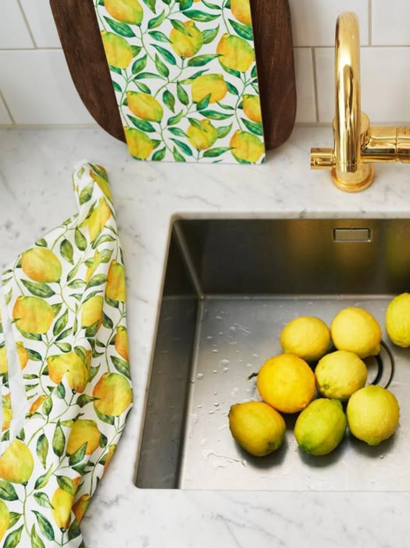 Kitchen sink with lemons and lemon-patterned towels on a marble countertop.