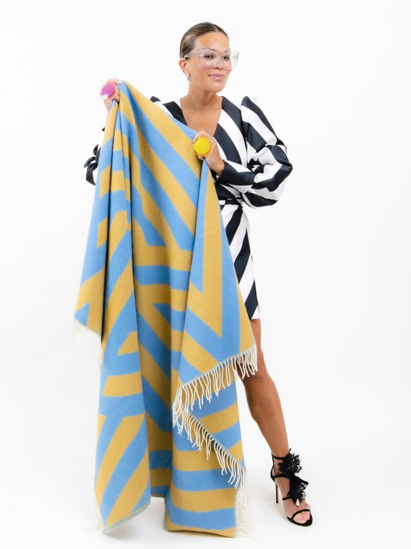 Woman standing and holding a blue and yellow diamond patterned wool blanket on a white background