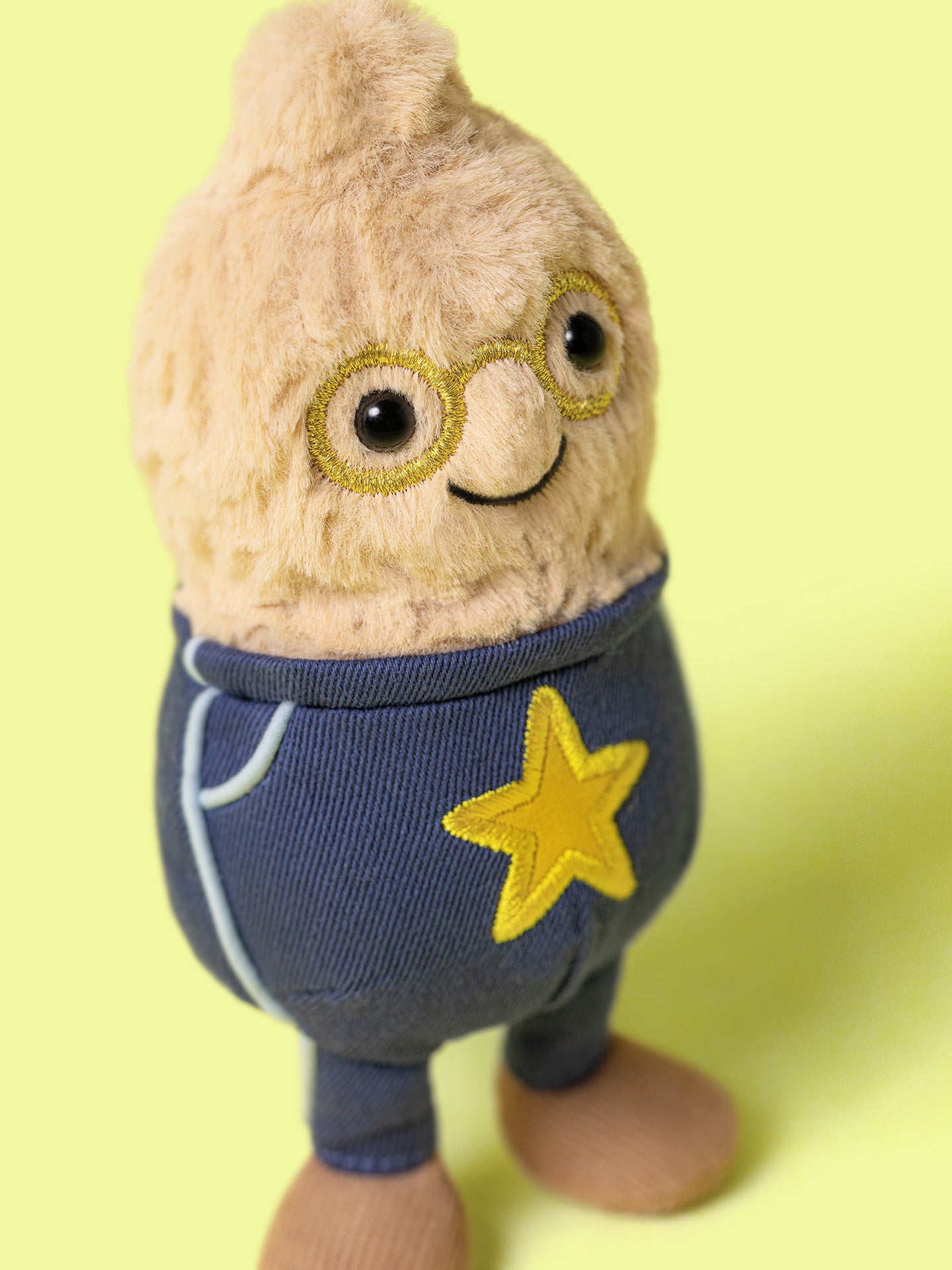 Stuffed toy peanut with a glasses and blue pants with a yellow star on a light green background
