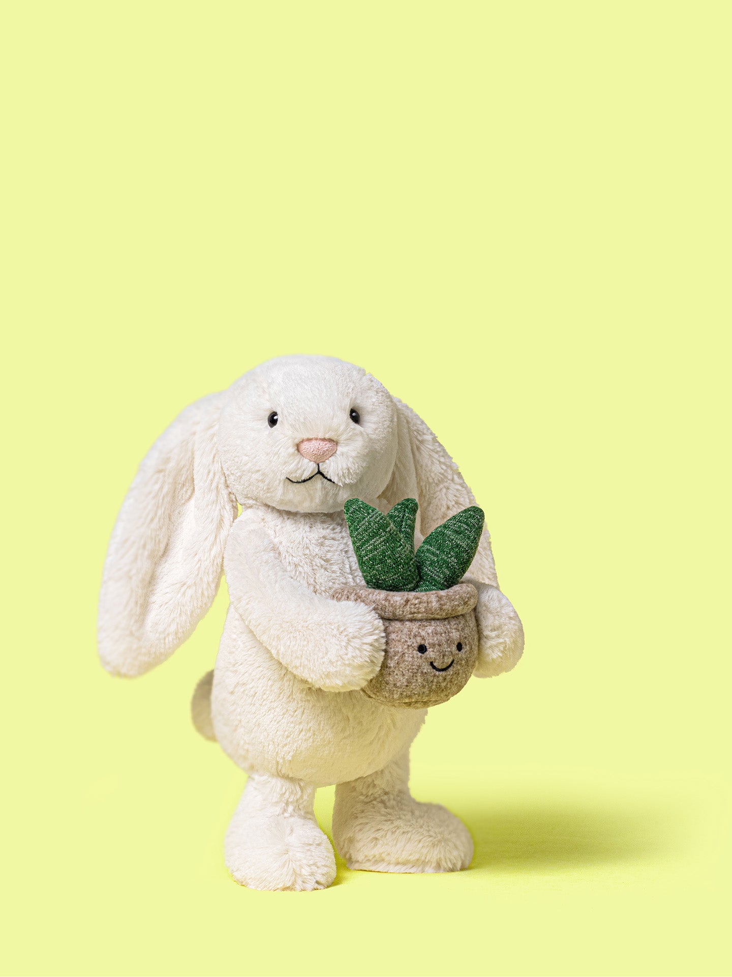 Stuffed bunny holding a potted plant on a yellow background but please note that the bunny soft toy can't stand on its' own in reality