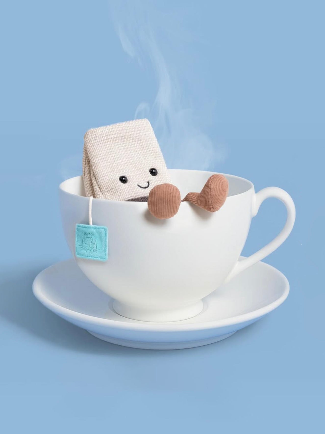 Toy tea bag character in a teacup with steam on a blue background