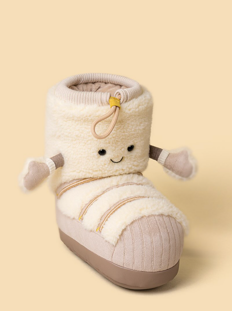 A plush character bootie in cream and beige, featuring a smiling face, small arms, and a ribbed sole, set against a solid pale yellow background.
