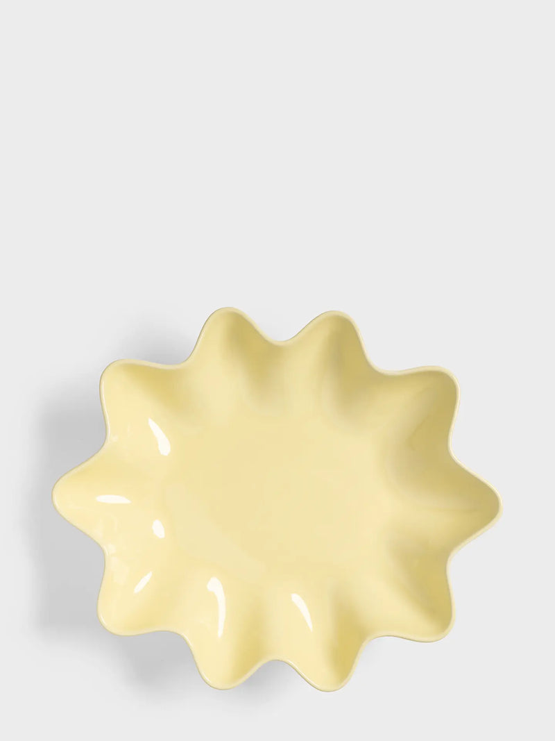 A pale yellow ceramic dish with a scalloped, starburst-like rim, photographed from directly above on a light gray background.