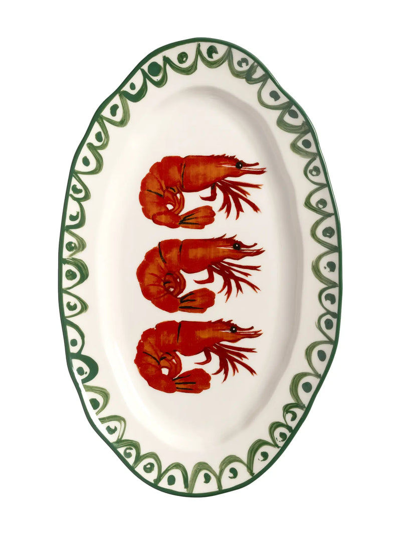An oval white ceramic serving platter featuring three red prawns stacked vertically in the center, surrounded by a green patterned border on a white background.
