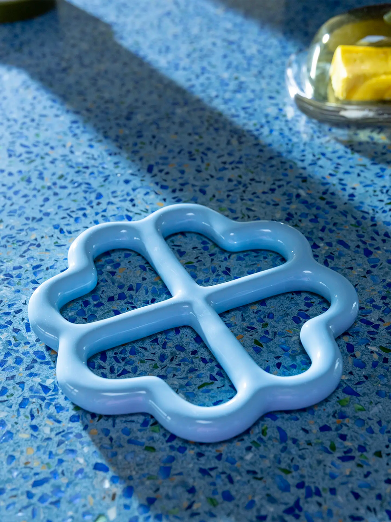 A light blue ceramic four-armed trivet, shown on a blue speckled terrazzo countertop.