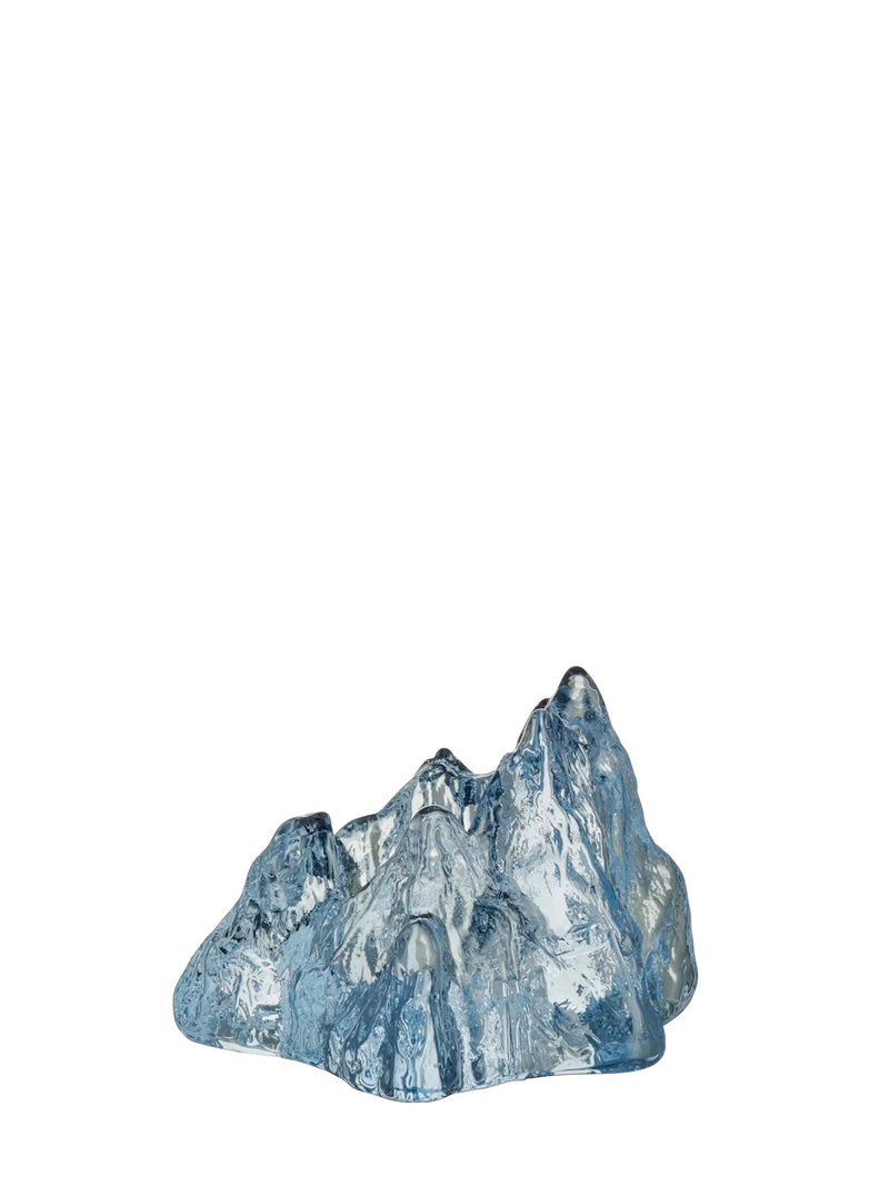 A small decorative mountain-shaped candle holder with a translucent textured surface reflecting green and white light from the ice blue glass, photographed on a plain white background