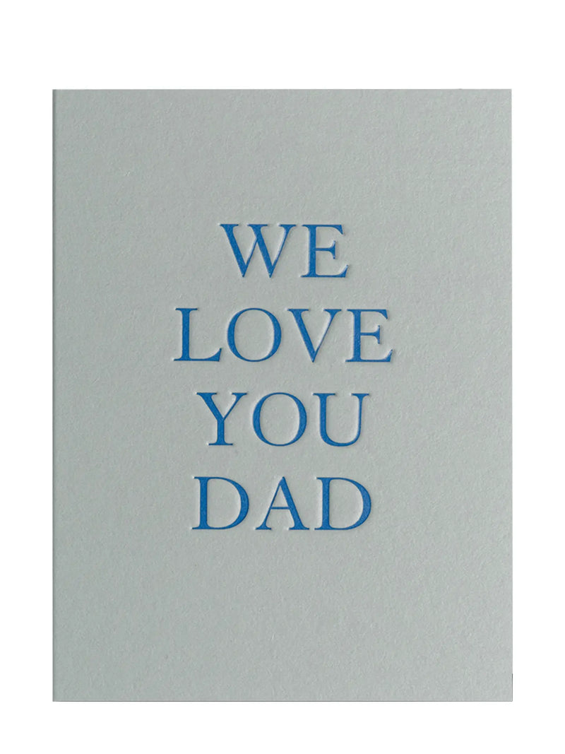 A minimalist greeting card with a light gray background and blue text reading 'WE LOVE YOU DAD' centered on the front.