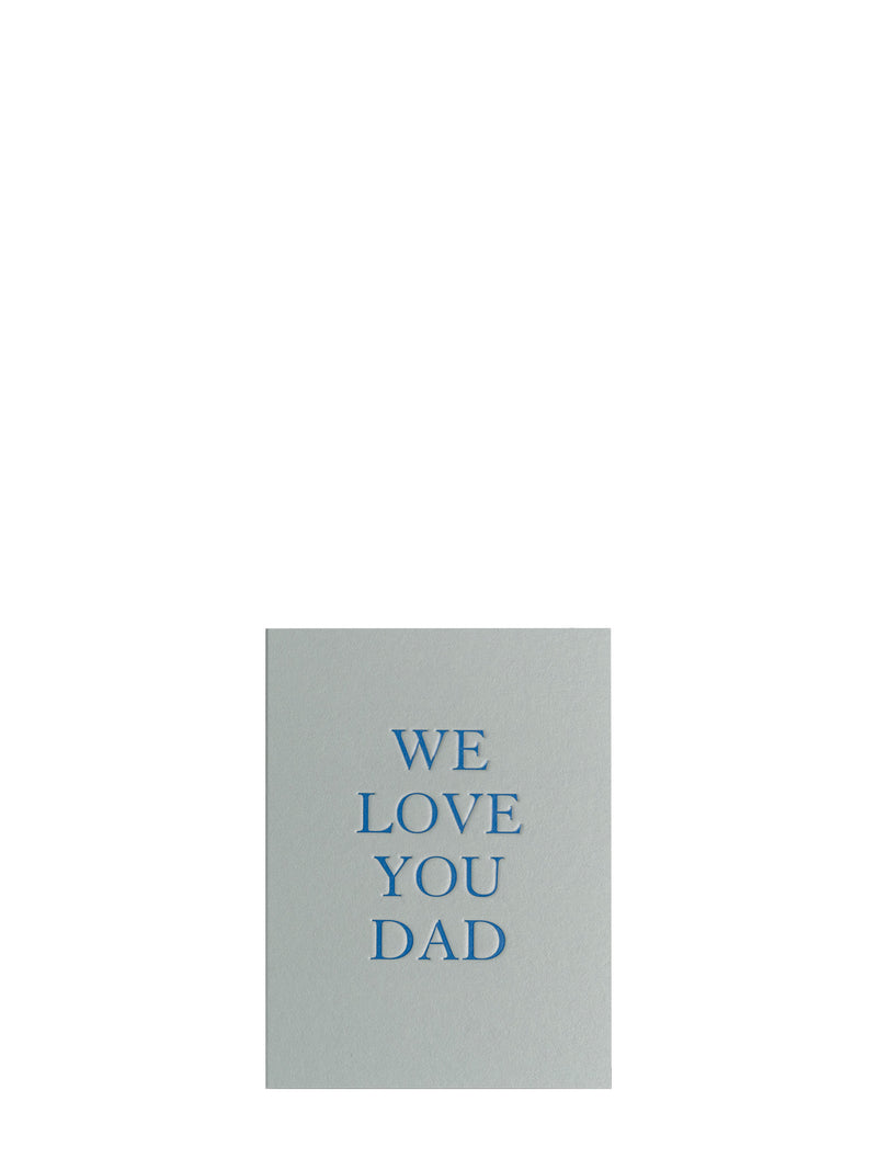 A minimalist greeting card with a light gray background and blue text reading 'WE LOVE YOU DAD' centered on a plain white background.