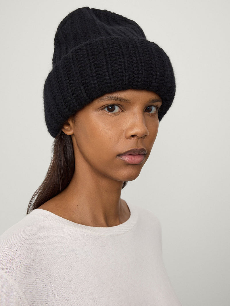 Woman wearing a black knit beanie against a plain background