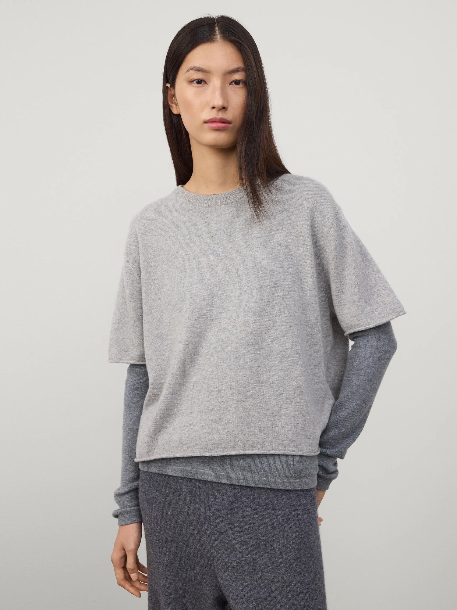 Woman wearing a gray sweater and pants on a plain background