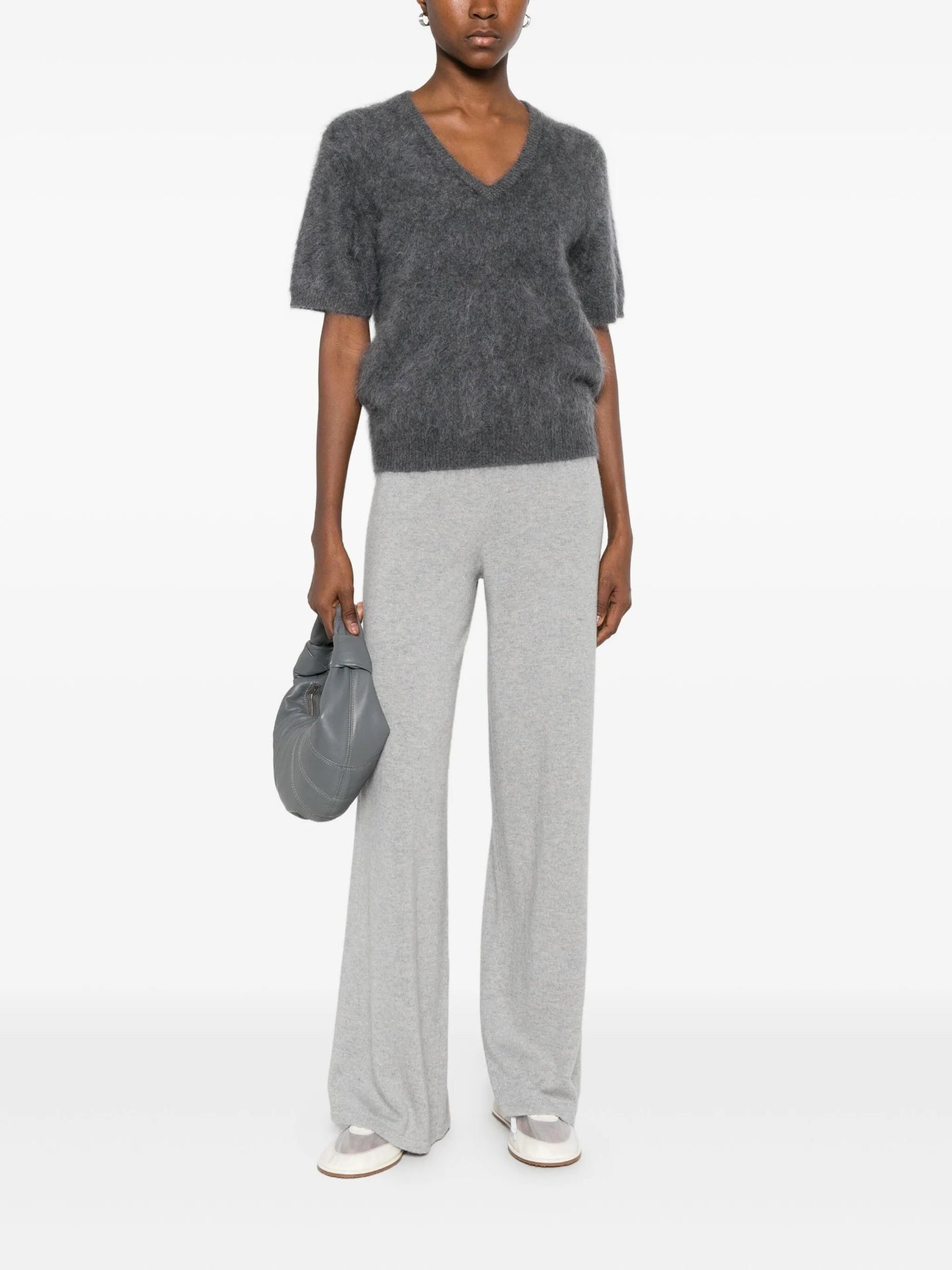 Person wearing a gray sweater and pants with a gray bag on a white background