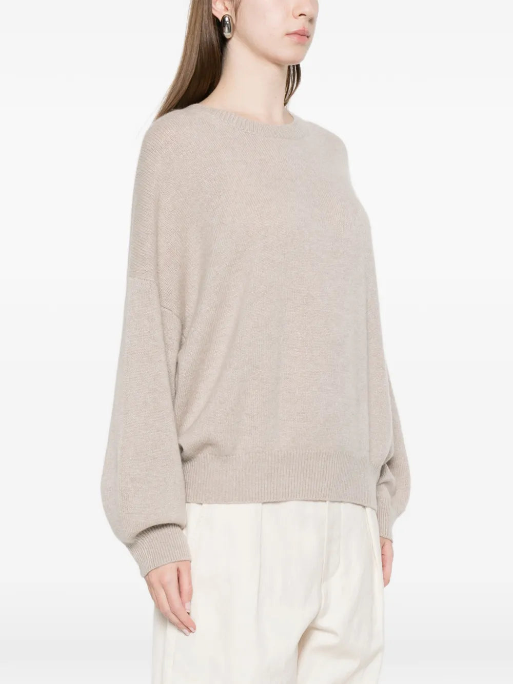 Person wearing a beige sweater and white pants on a white background
