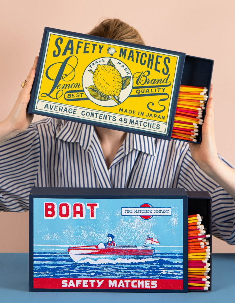 Two boxes of safety matches with vintage designs held by a person.