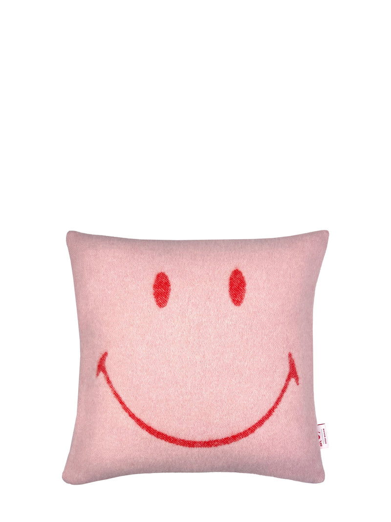 A square pink cushion with a simple red smiley face design on the front, photographed against a solid white background.