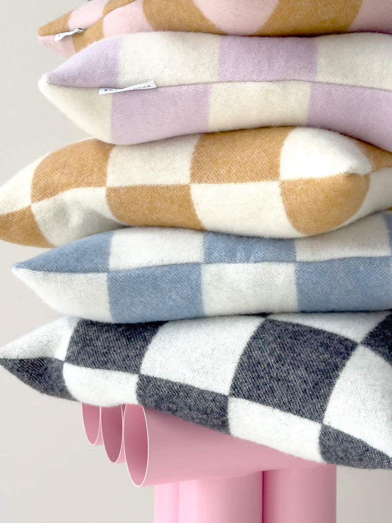 A stack of five wool throw pillows in different checkered patterns, displayed on a pink stand against a light gray background.