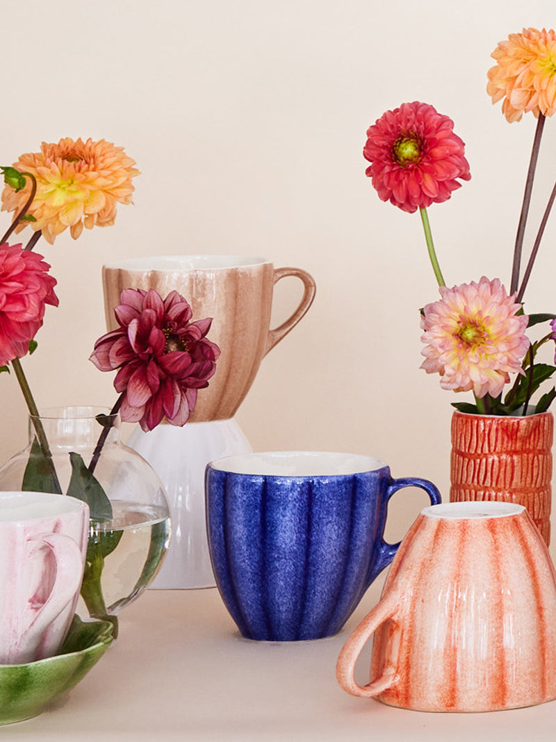 Colorful mugs and vases with flowers on a light background