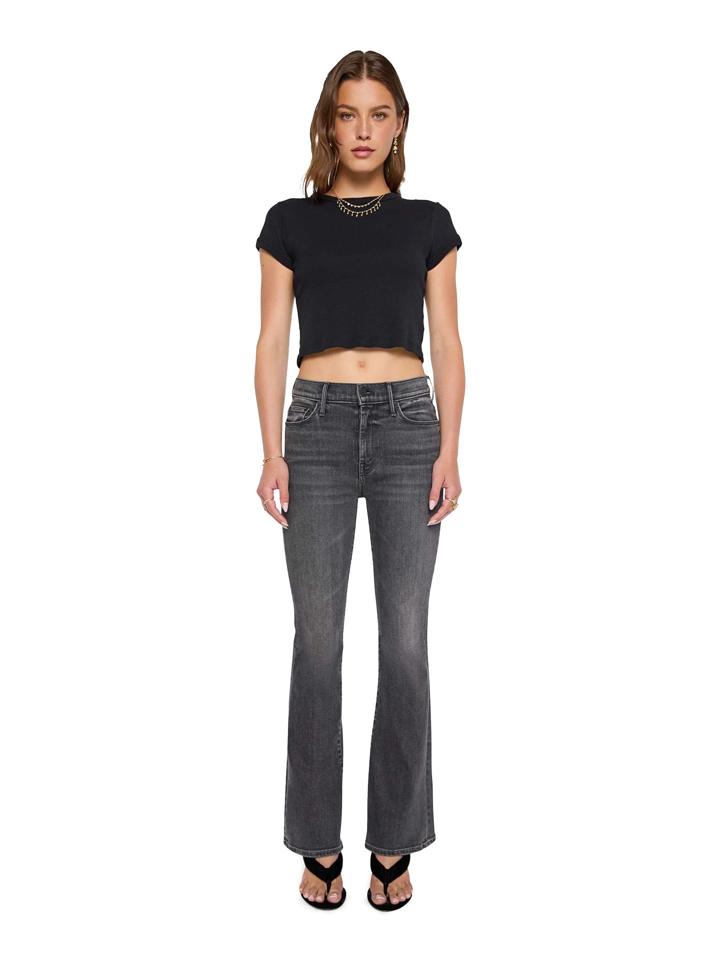 Woman wearing a black crop top and gray flared Mother jeans on a white background