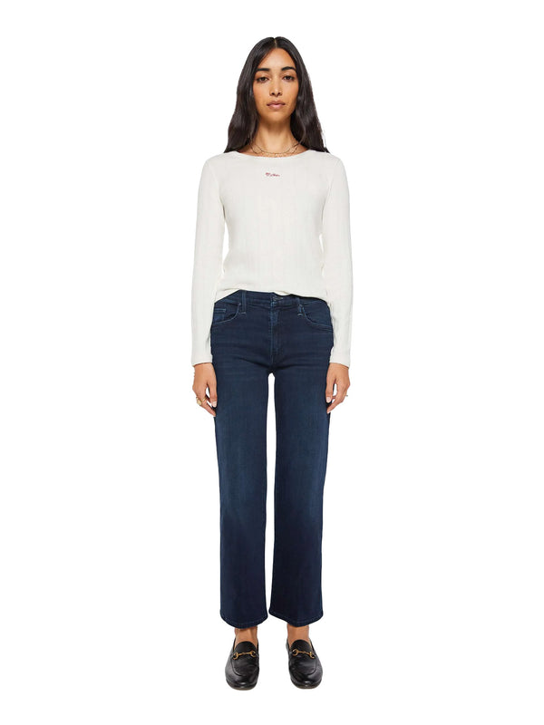 A woman modeling a white long-sleeve knit top and dark blue cropped jeans with black loafers, standing against a plain white background.