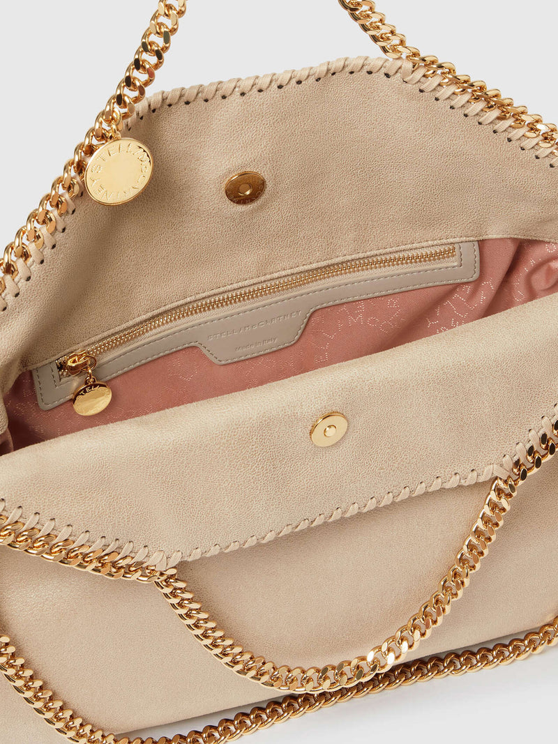 Close-up of the interior of a beige vegan suede shoulder bag with gold-tone chain straps, a zippered pocket, and a pink Stella McCartney logo patterned interior lining.