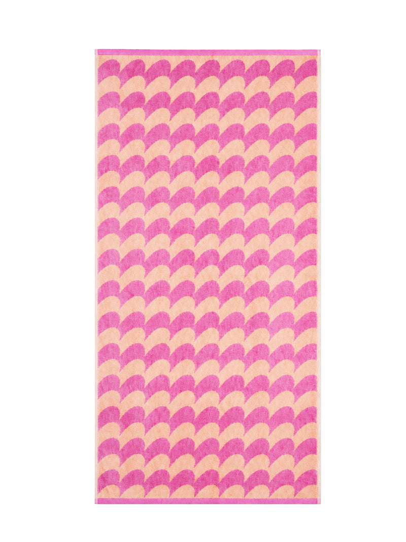 A rectangular 140 x 70 cm sized bath towel featuring a repeating curvy mountain row o or fan pattern in alternating shades of pink and light peach on a white background.