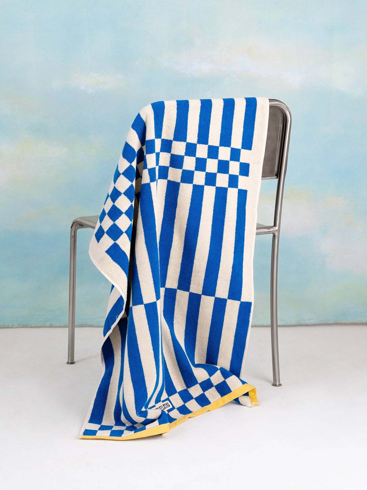Blue and white checkered towel draped over a chair with a beach scene in the background