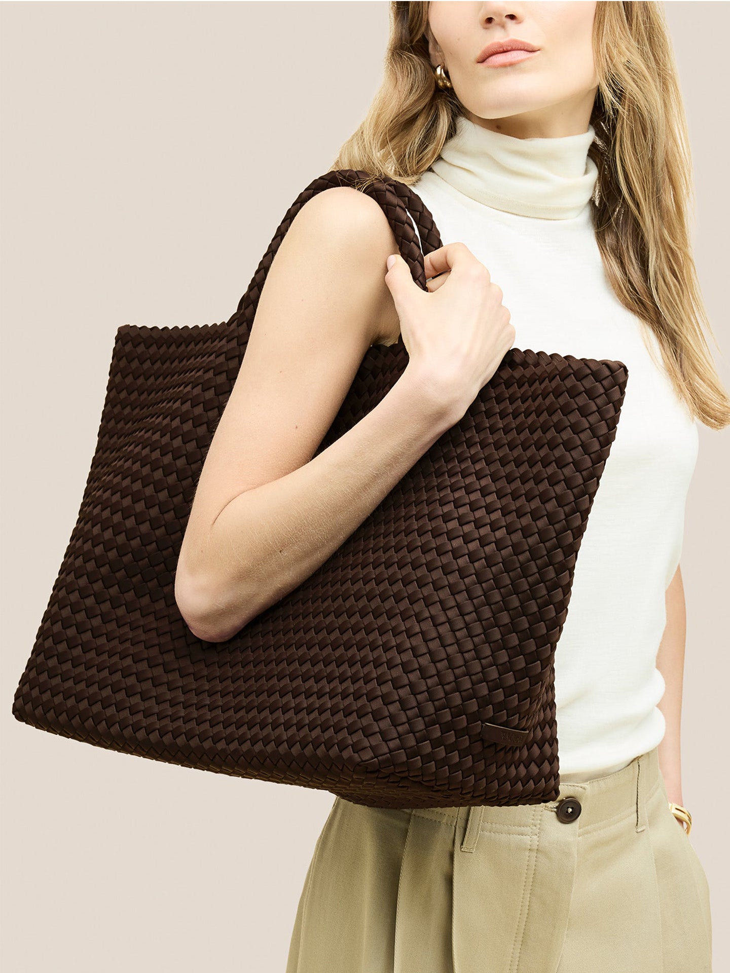 Woman holding a brown woven handbag against a neutral background