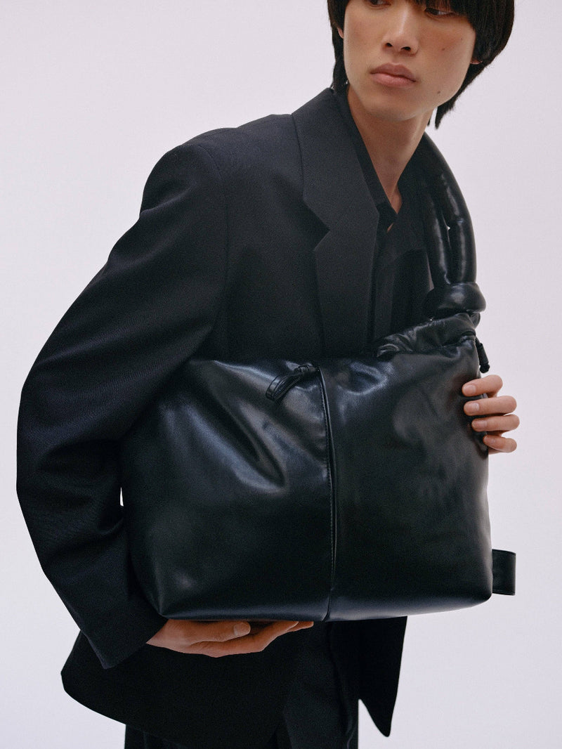 Person holding a black leather bag against a plain background