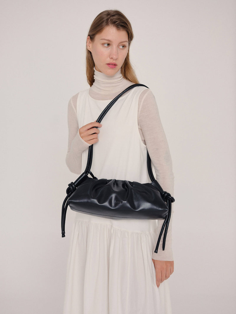 Woman holding a black leather shoulder bag on her shoulder against a plain background