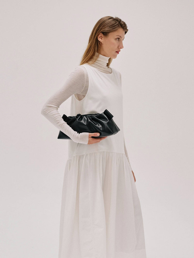Woman in a white outfit holding a black clutch against a plain background