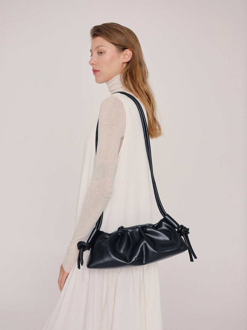 Woman carrying a black handbag on one shoulder againt a plain background